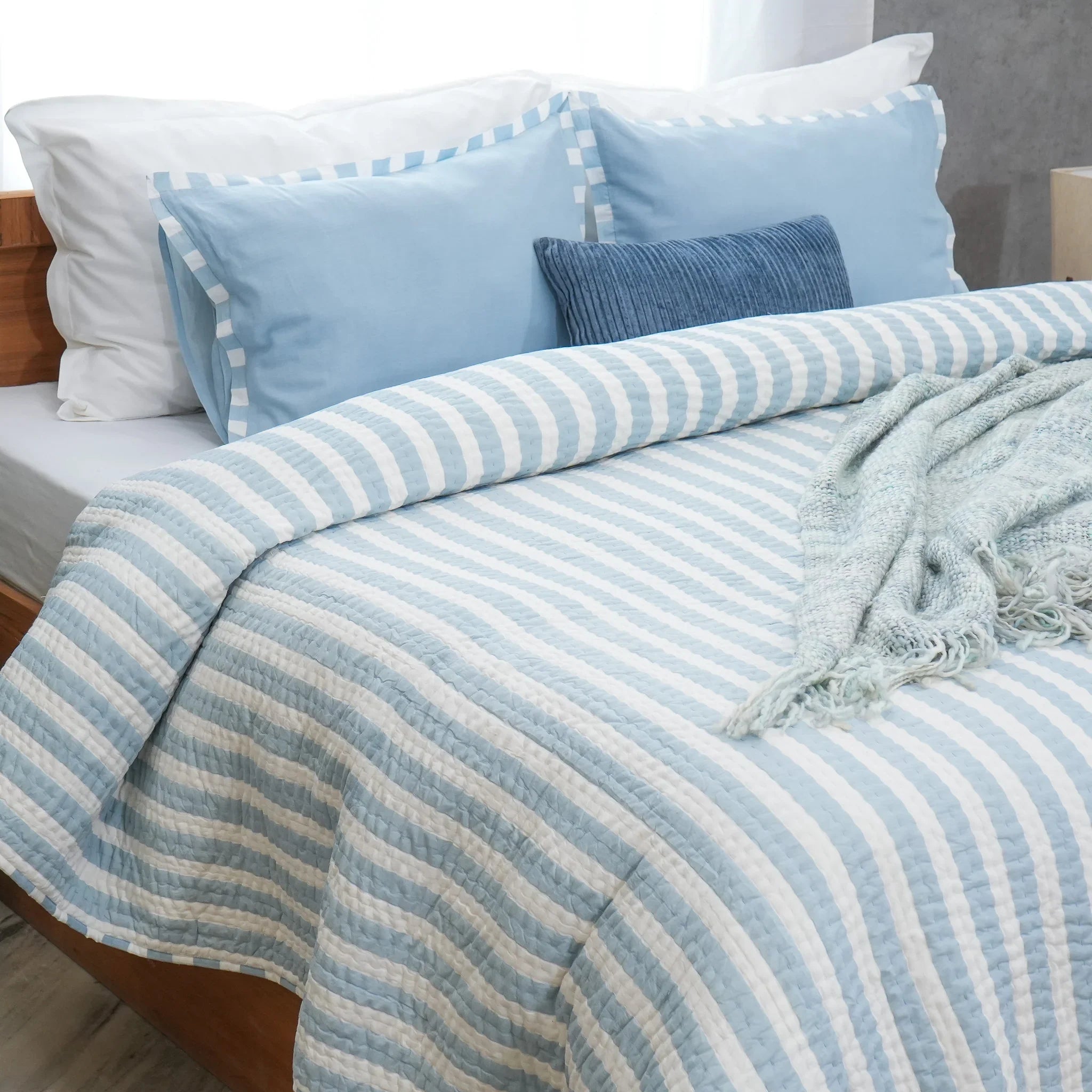 Blue and white striped cotton quilt styled on a bed with matching pillows