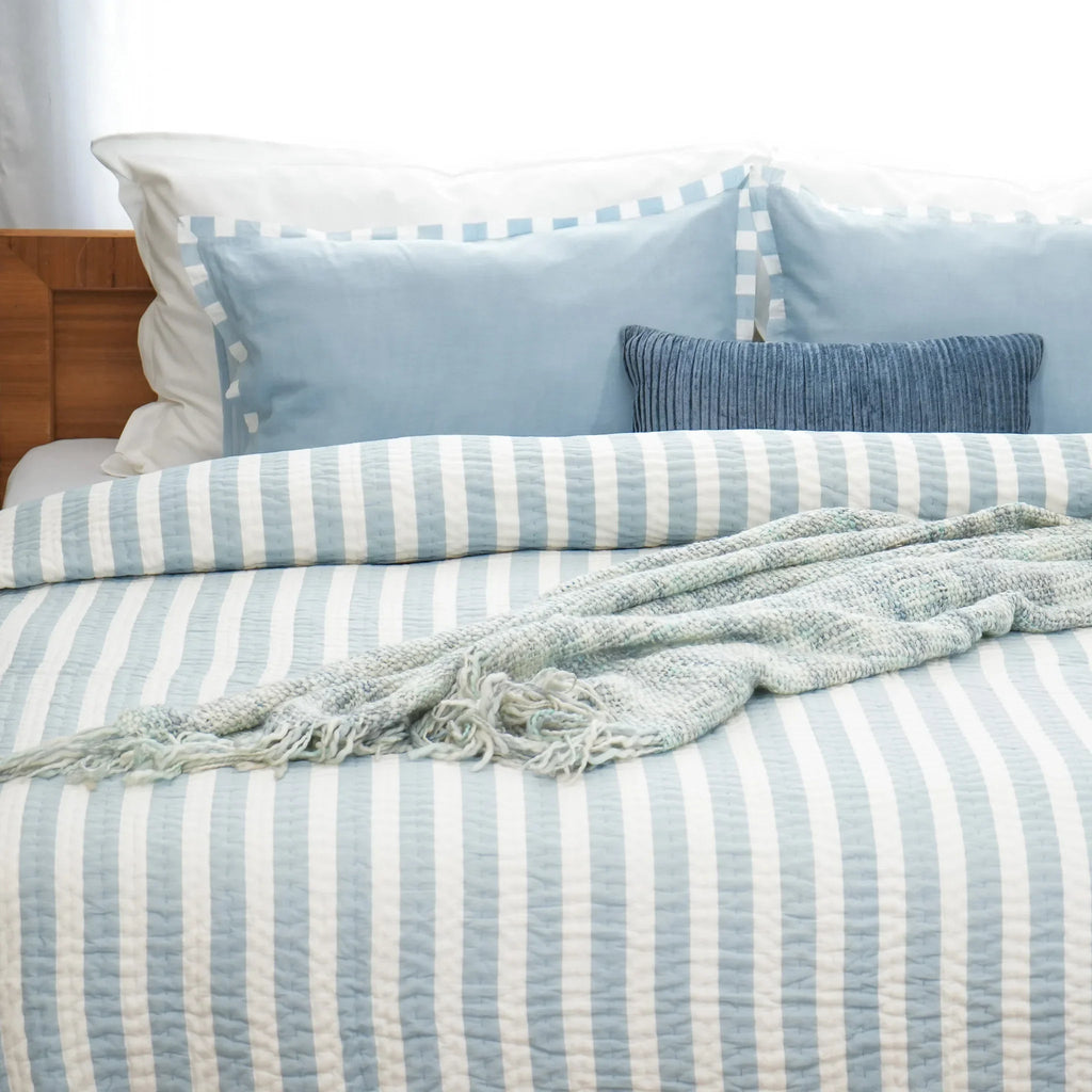 Side view of blue and white striped cotton quilt with matching pillows