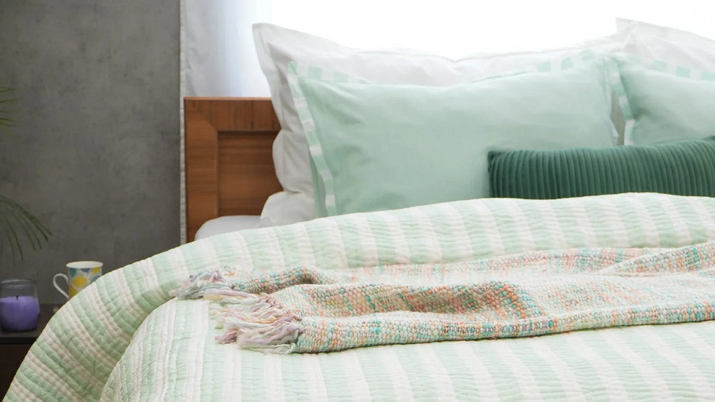 Green and white striped cotton quilt folded at the foot of a neatly made bed