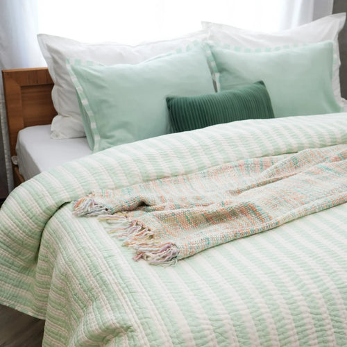 Mellow green and white striped cotton quilt styled on a bed with matching pillows