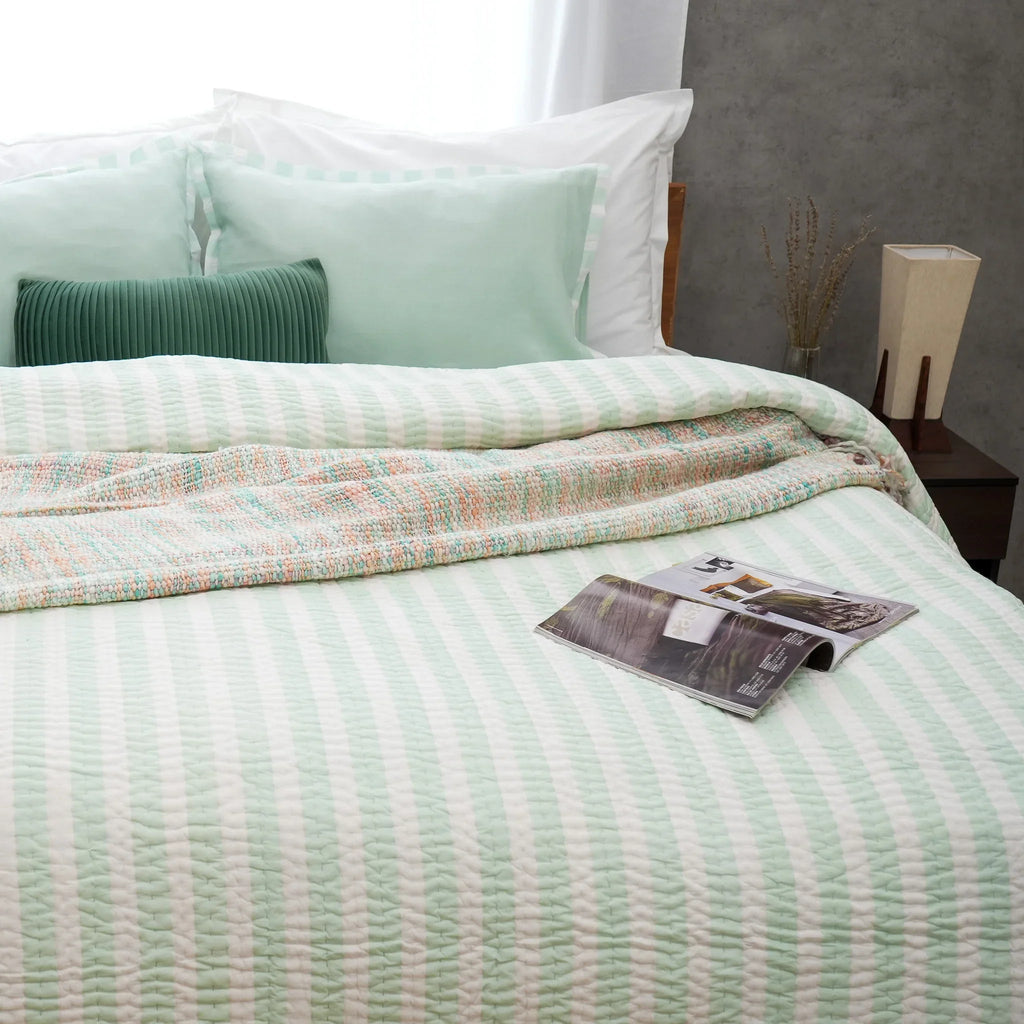 Green and white striped cotton quilt styled with a book on the bed
