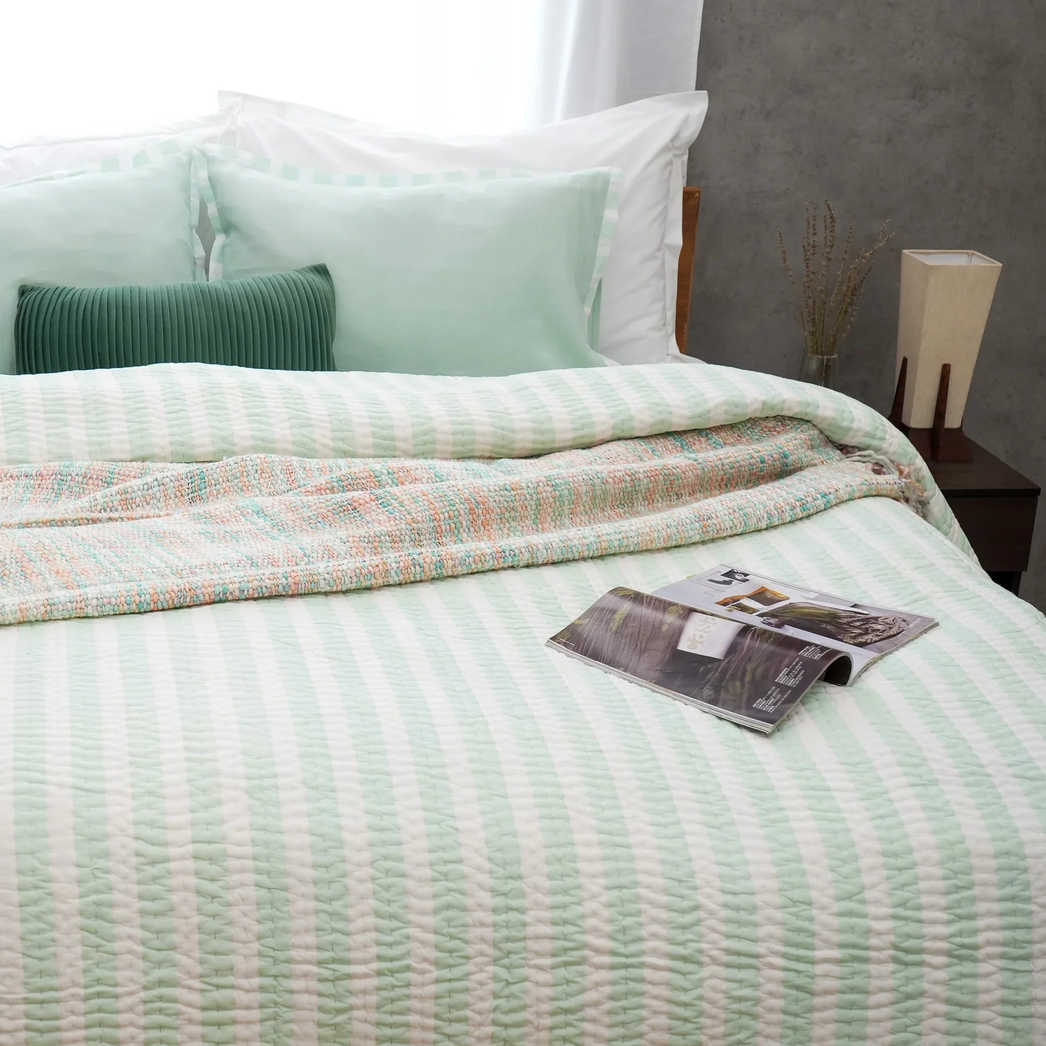 Green and white striped cotton quilt styled with a book on the bed