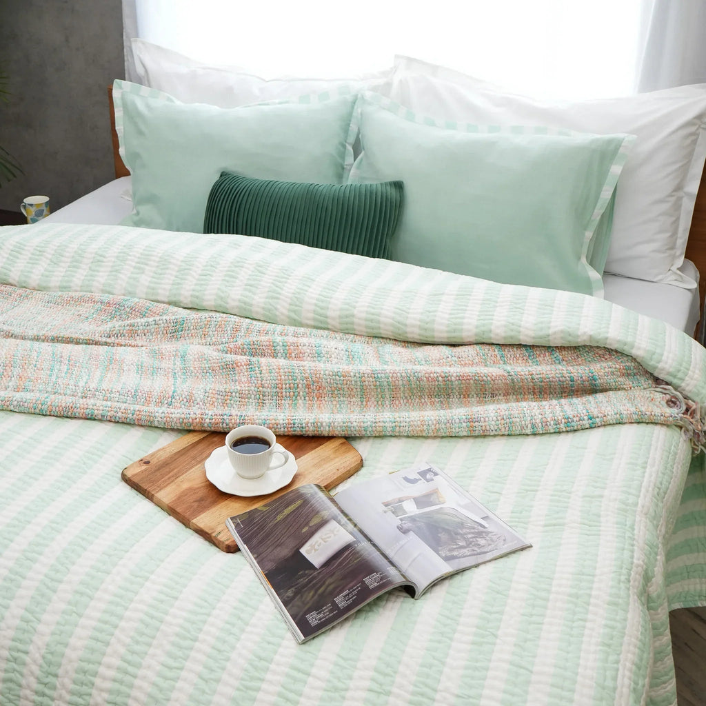 Green and white striped cotton quilt styled with a book and decorative accessories
