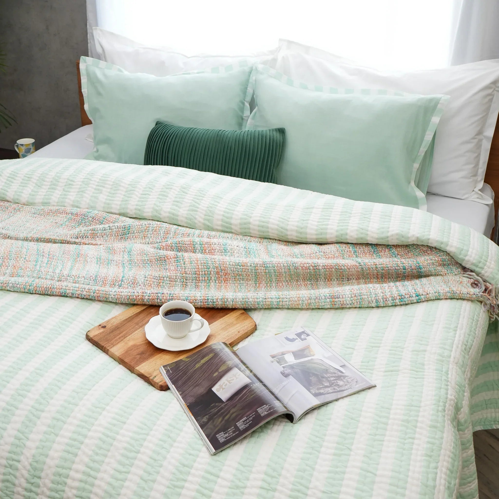 Green and white striped cotton quilt styled with a book and decorative accessories