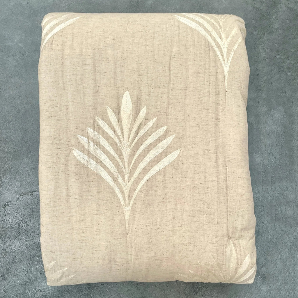 Flat lay of natural embroidered cotton-linen quilt showing palm embroidery