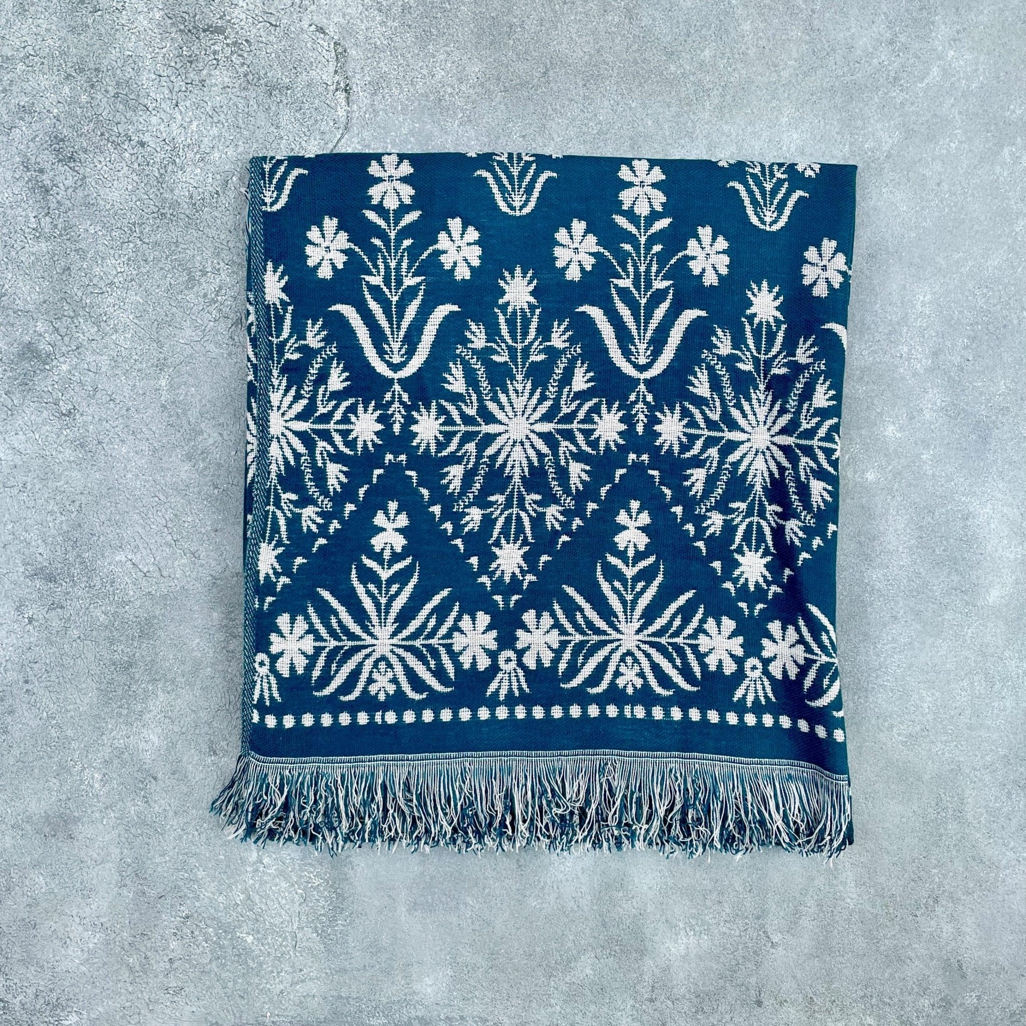 Flat lay of blue jacquard floral throw on grey textured background