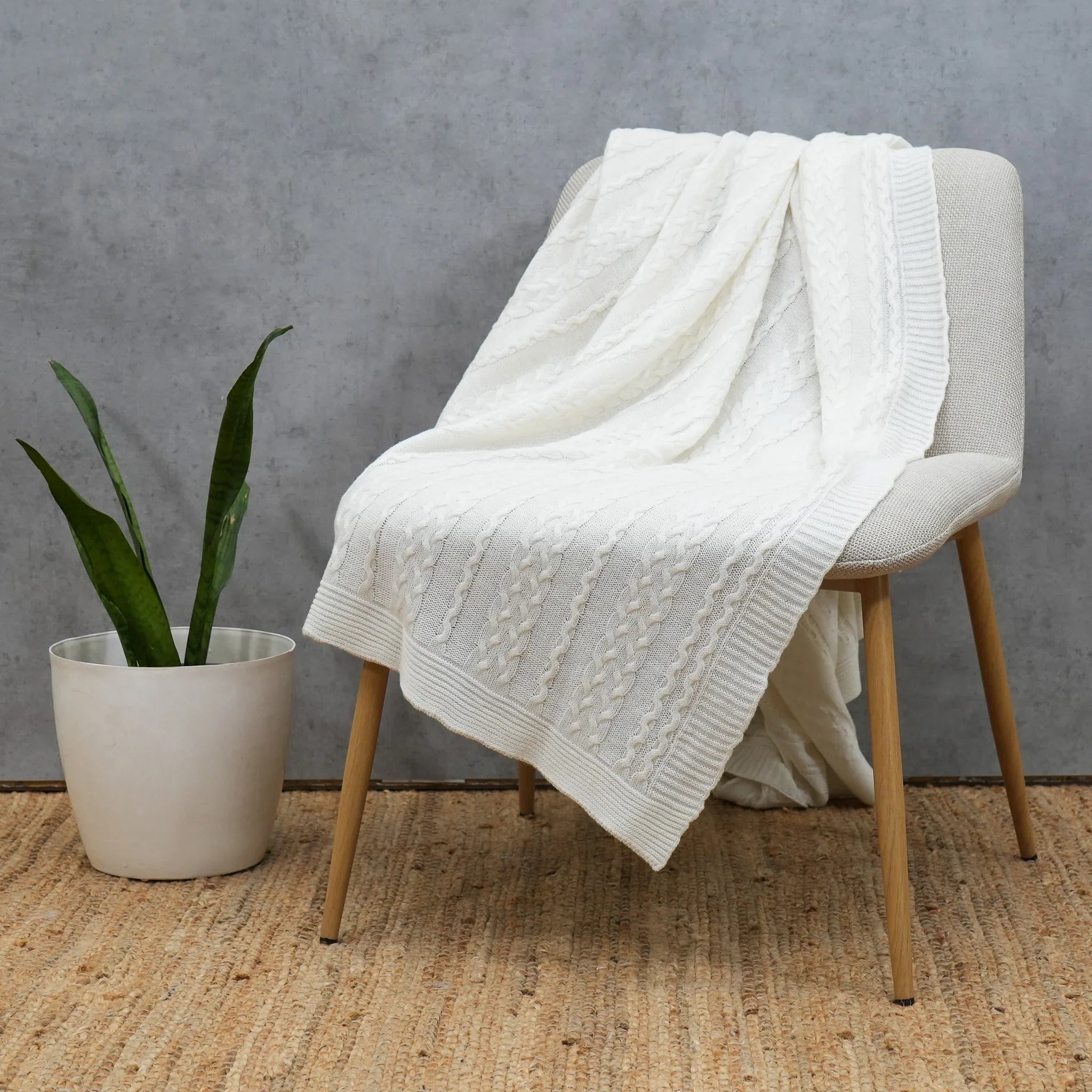 Ivory cable knit cotton throw draped over a wooden accent chair