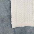 Folded ivory cotton cable knit throw on grey background