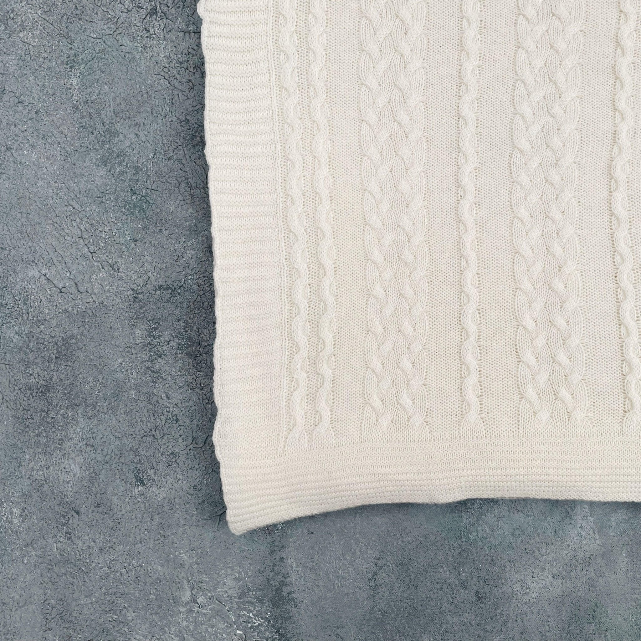 Folded ivory cotton cable knit throw on grey background