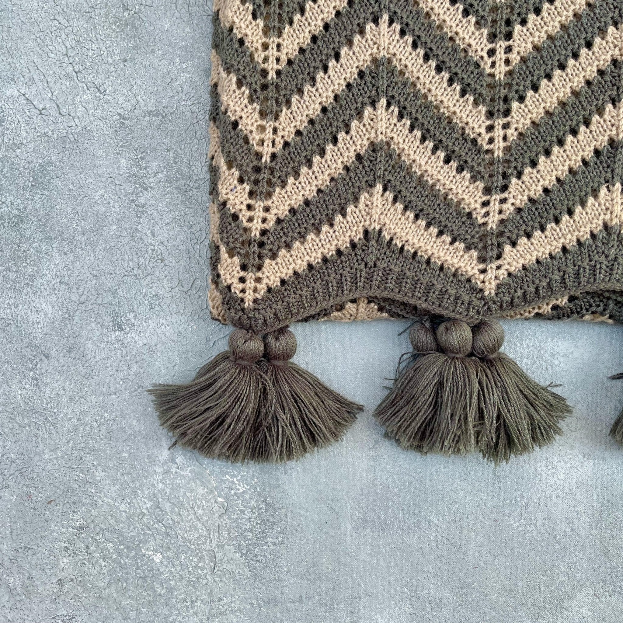 Close-up of grey and beige acrylic crochet throw with chevron weave and tassels