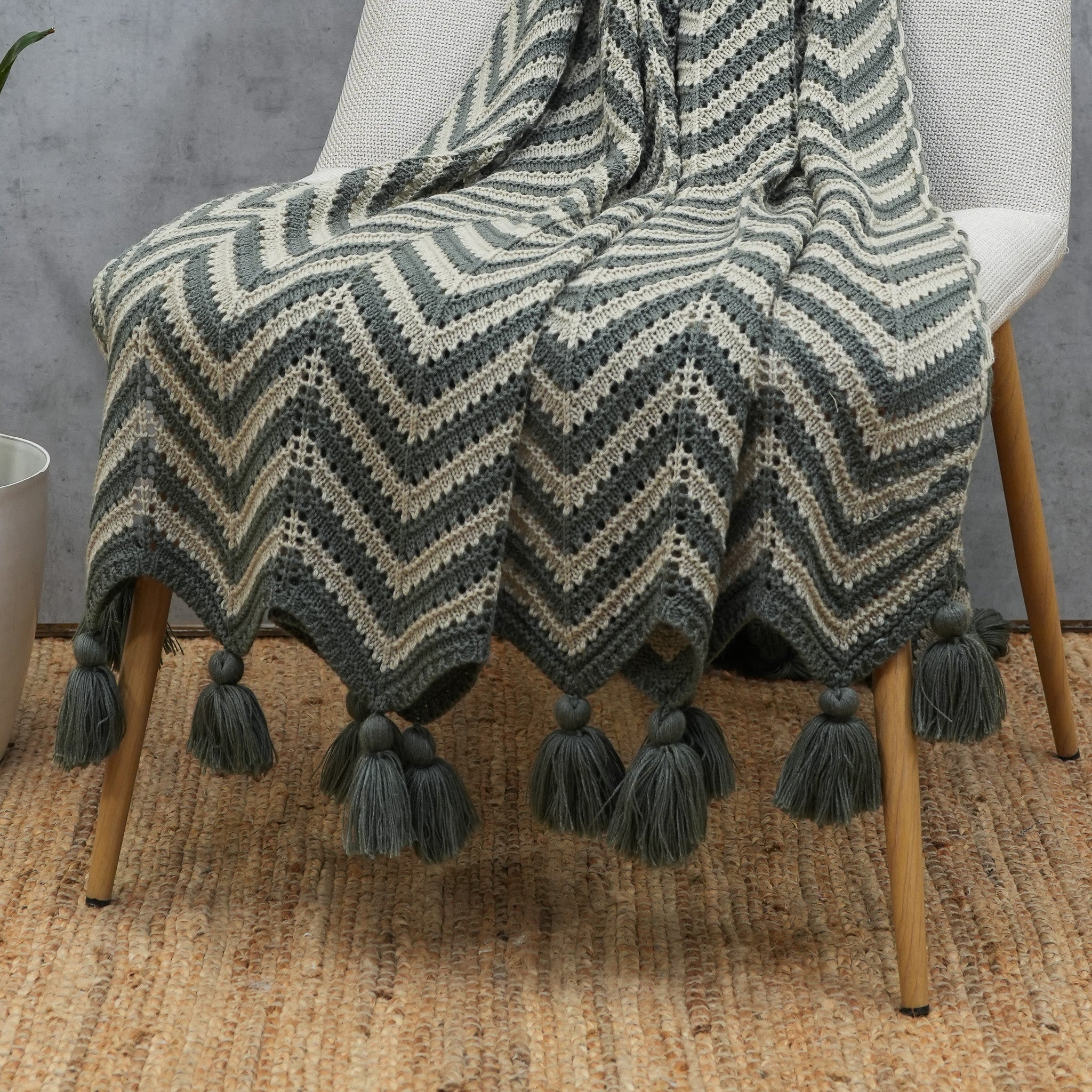 Grey and beige crochet acrylic throw with tassels draped over a chair
