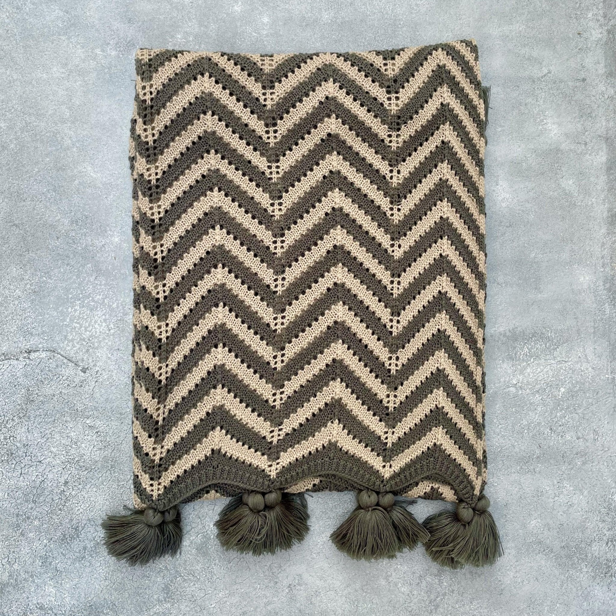 Flat lay of grey and beige crochet acrylic throw on grey textured background