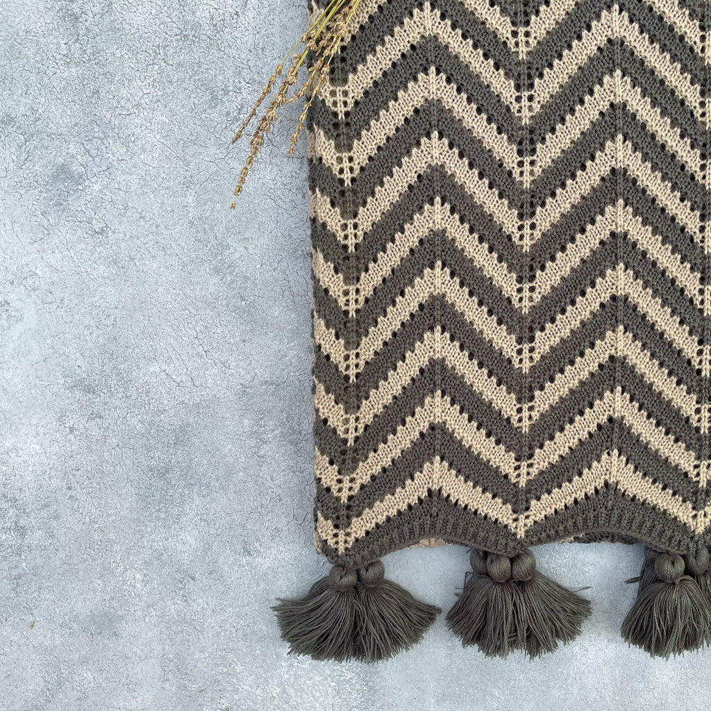 Corner detail of grey and beige crochet acrylic throw with tassel fringe